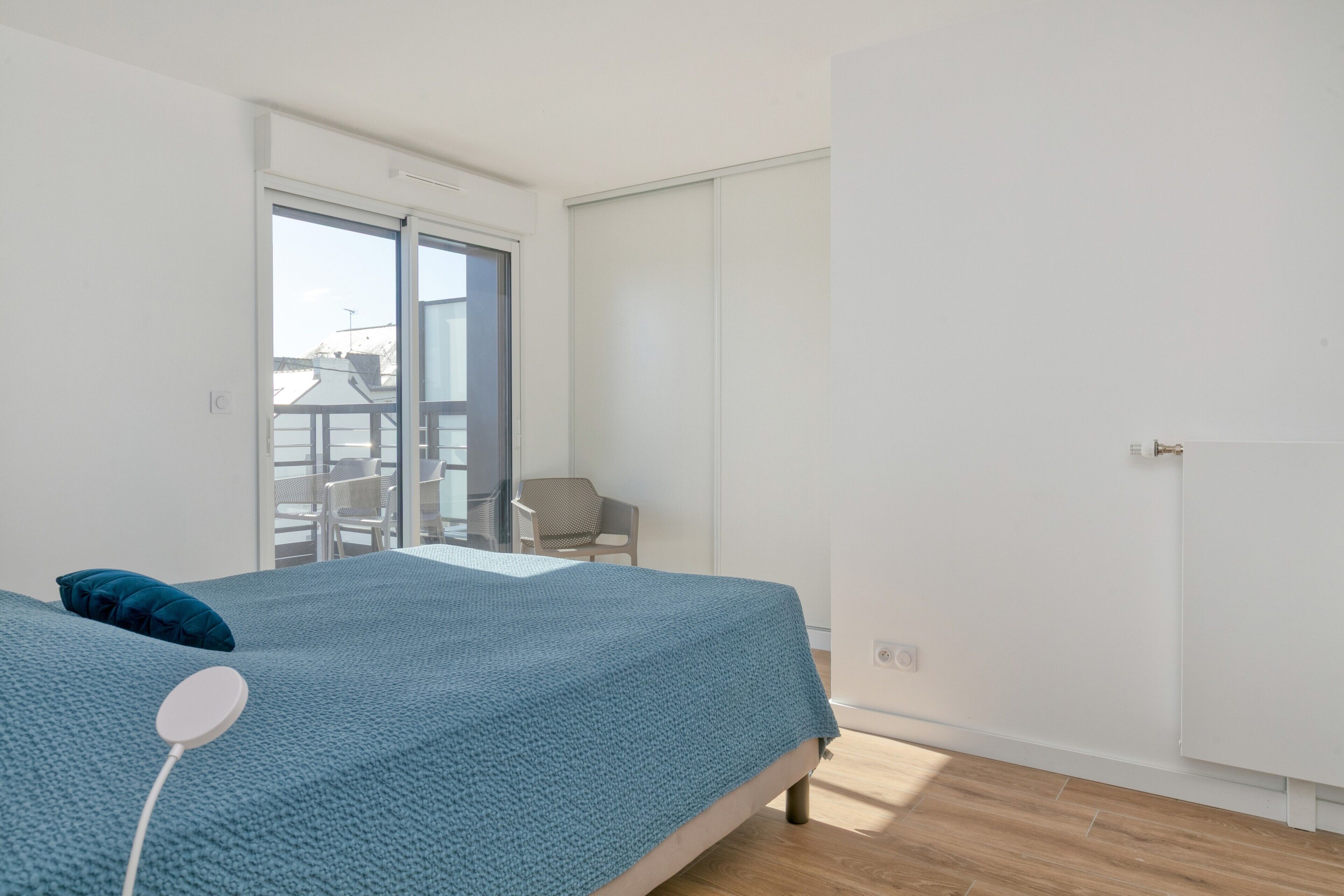 A bedroom with a bed, a chair, a wardrobe, and a view of the outside.
