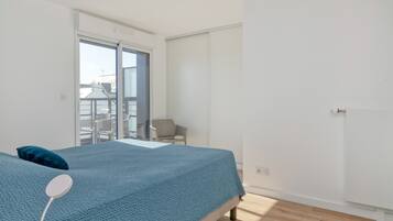 A bedroom with a bed, a chair, a wardrobe, and a view of the outside.