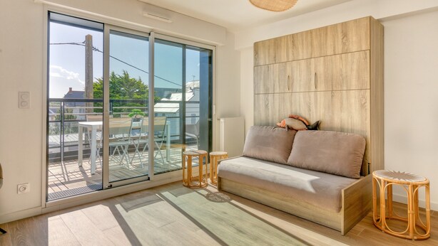 A modern living room with a sofa, a glass door leading to an outdoor balcony, and a ceiling fan. - Apartment 'Port Lin Near the Ocean' with Balcony and Wi-Fi (Le Croisic)