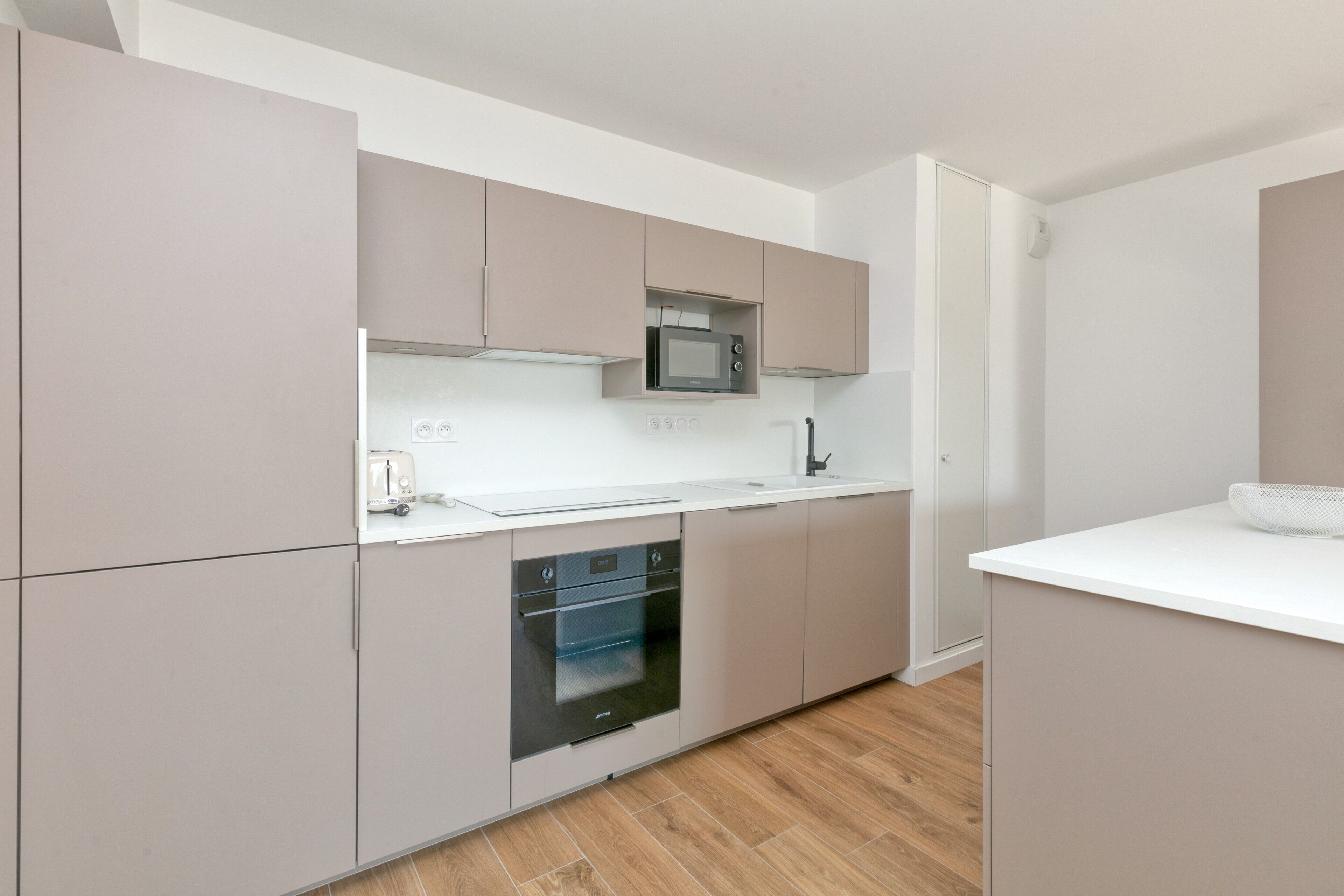 A modern kitchen with built-in appliances, a white countertop, and light wood flooring.