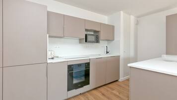 A modern kitchen with built-in appliances, a white countertop, and light wood flooring.