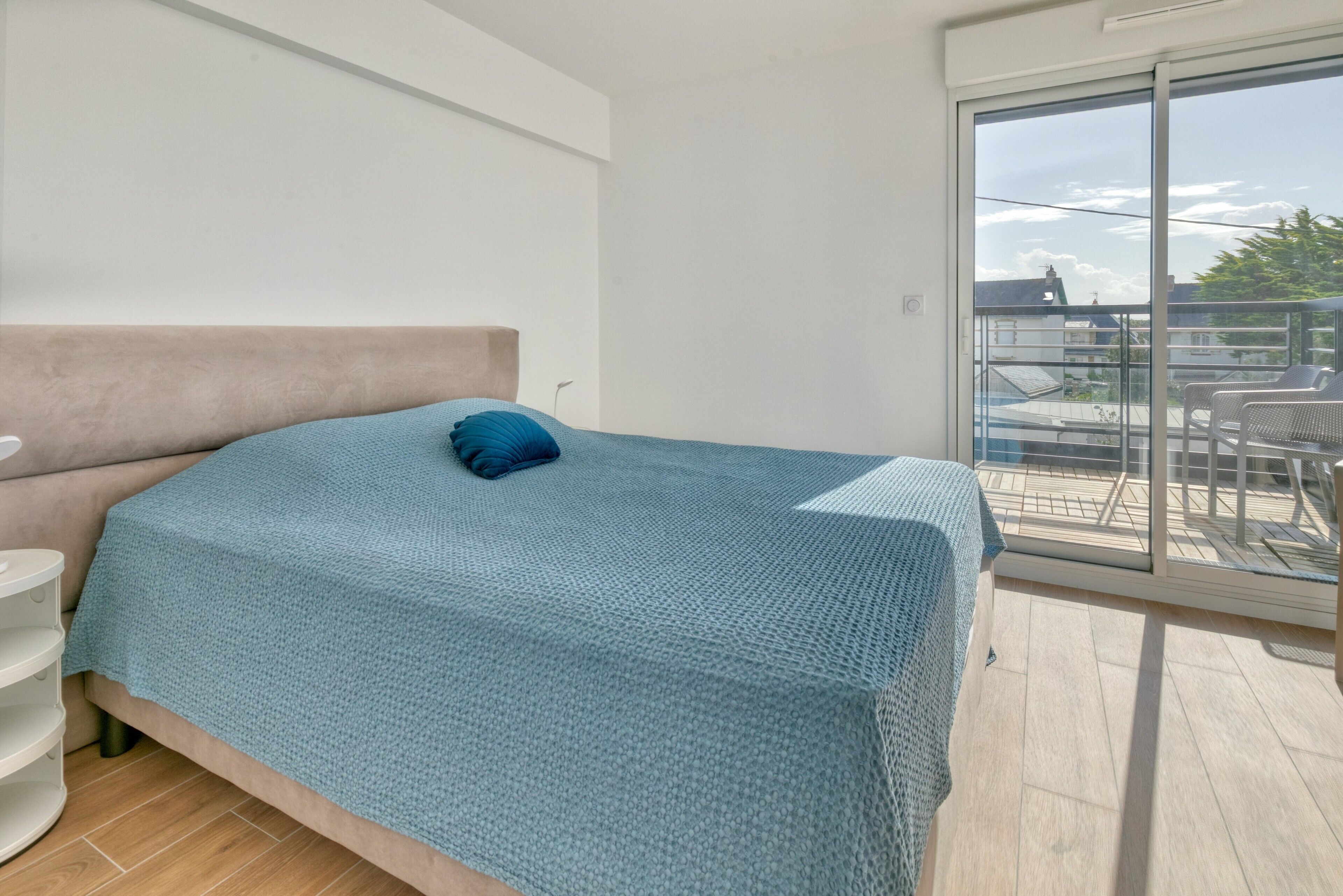 A bedroom with a bed, a blue pillow, a white bedside table, and a sliding glass door leading to a balcony.