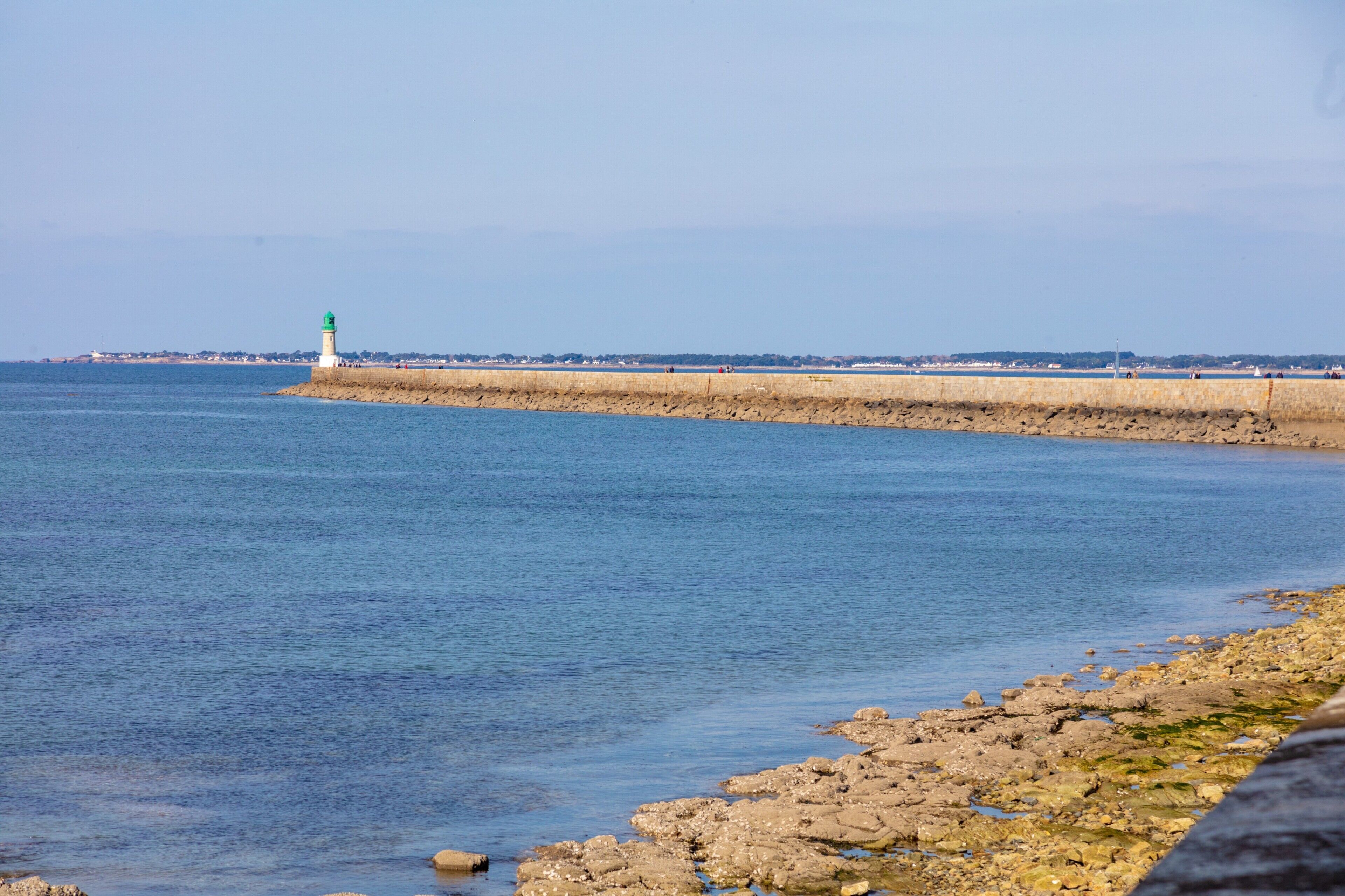 Eine Küstenansicht mit einem Leuchtturm, felsiger Küstenlinie und einer ferngesiedelten Stadtlandschaft.