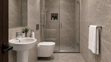 Un baño moderno con ducha envuelta en vidrio, un lavamanos blanco y un inodoro.