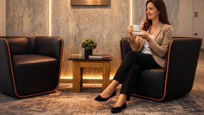 Ein modernes Interieur mit zwei schwarzen Stühlen, einem kleinen Holztisch mit einer Pflanze und einer Wandleuchte.