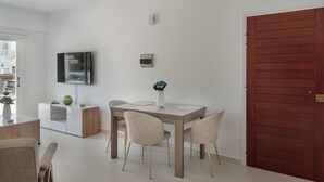 Ein stilvoller Essbereich mit einem Holztisch, vier Stühlen, einem weißen Schrank, einem an der Wand befestigten Flachbildfernseher und einer roten Tür.