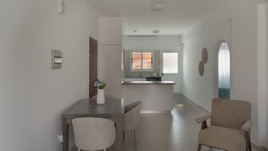 Ein moderner Essbereich mit einem Holztisch und zwei Stühlen, im Hintergrund eine Küche und durch einen Bogen ein Blick in den Wohnbereich.