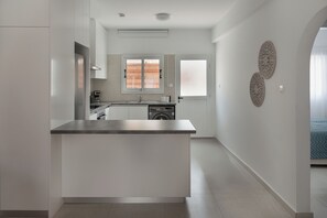 A modern kitchen with a central island, built-in appliances, and a view to a bedroom. - Phaedrus Living Olga Residence (Paphos)