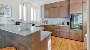 A modern kitchen with wooden cabinets, a marble countertop, and a built-in oven.