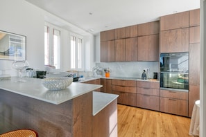 A modern kitchen with wooden cabinets, a marble countertop, and a built-in oven. - Villa 'Lin Et Maree Face Océan' with Sea View, Private Garden and Wi-Fi (Croisic)
