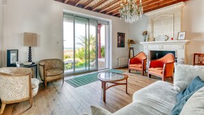 A spacious living room with a fireplace, wooden ceiling beams, and a large sliding glass door leading to a balcony.