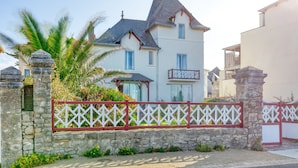 A large, two-story house with a stone wall and a red and white fence.