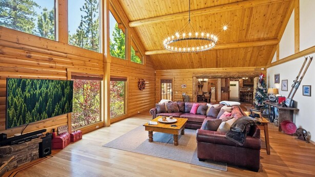 Un interior de cabaña espacioso con un alto techo de madera, una zona de estar acogedora con un sofá y sillones, un televisor y una chimenea.
