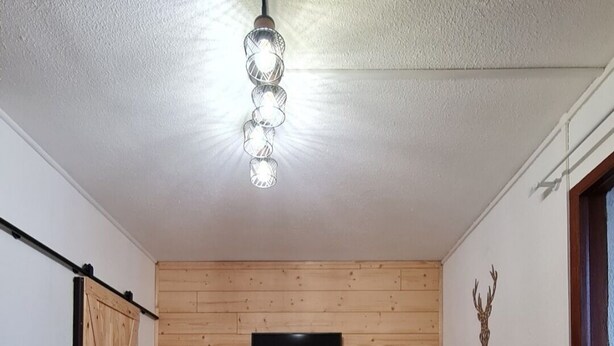 A room with a wooden floor, a dining table with benches, a mounted TV, and a ceiling light fixture. - Studio Cozy in Pyrénées 2000 (Bolquère)