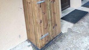 A wooden wardrobe with metal handles and a latch, positioned against a beige wall with a dark door in the background. - Studio Cozy in Pyrénées 2000 (Bolquère)