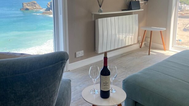 Una stanza con vista sul mare, una TV fissata al muro, una bottiglia di vino e due bicchieri su un tavolino.