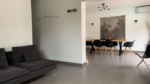 A modern living room with a dark grey sofa, a dining area with a wooden table and black chairs, and a large abstract painting on the wall.