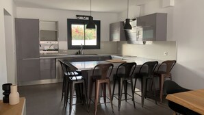 A modern kitchen with grey cabinets, a central island with bar stools, and a window with a view of greenery.