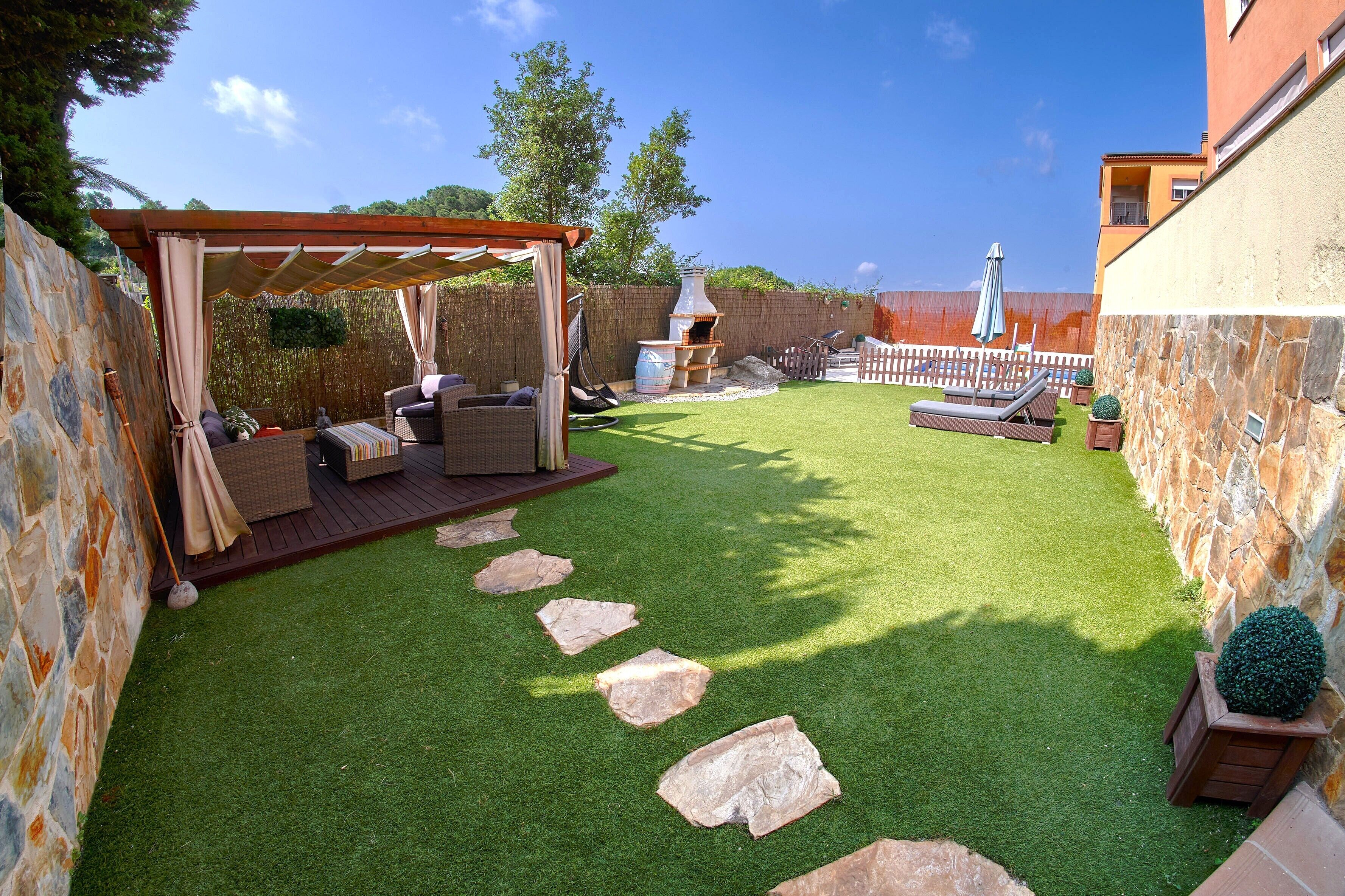 A backyard with a pergola, outdoor seating, a barbecue area, and a stone wall.