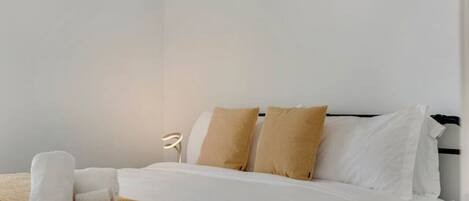 Un lit bien fait, avec une literie blanche et beige, une lampe de chevet et un luminaire fixé au mur.
