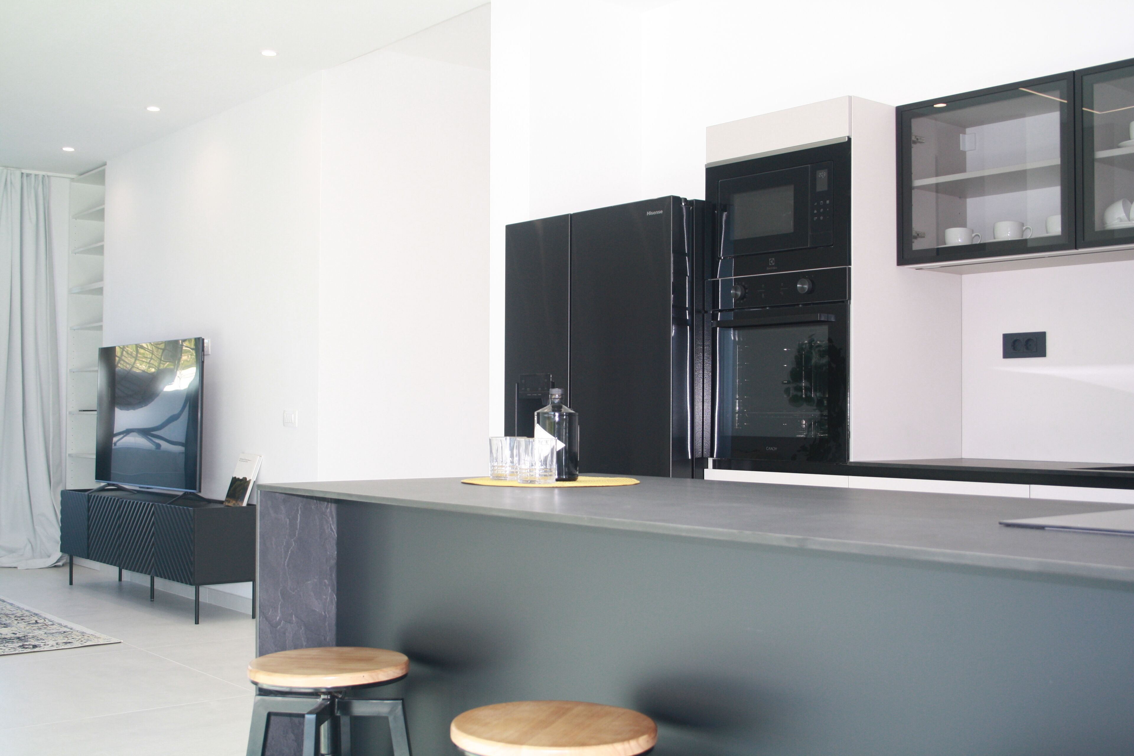 A modern kitchen with black appliances, a grey countertop, and two wooden stools.