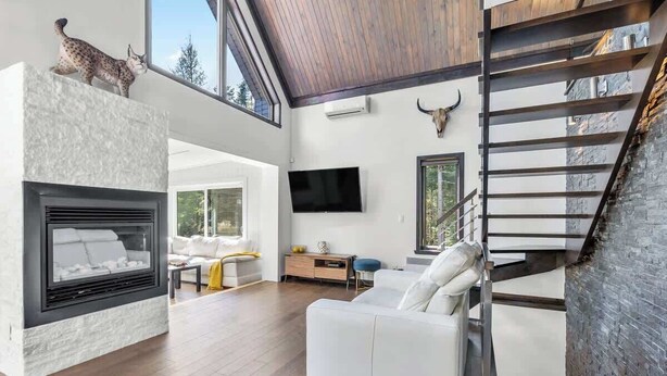 A modern living room with a fireplace, a sofa, a TV, and a staircase. - Bora Nature | Private Spa & Lakefront (Shannon)