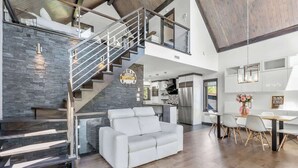 A modern living space with a staircase, a white sofa, a dining area, and a kitchen. - Bora Nature | Private Spa & Lakefront (Shannon)