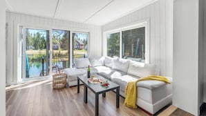 A modern living room with a white sofa, a coffee table, and a view of a lake and trees. - Bora Nature | Private Spa & Lakefront (Shannon)