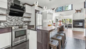 A modern kitchen with a central island, stainless steel appliances, and a large window overlooking a garden. - Bora Nature | Private Spa & Lakefront (Shannon)