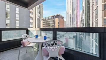 A balcony with a table and chairs, a view of high-rise buildings, and a glass railing.