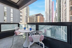A balcony with a table and chairs, a view of high-rise buildings, and a glass railing.