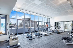 A modern gym with various cardio machines, large windows offering city views, and a spacious layout. - City View 2BR, FREE Parking, Bright & Central Apt (Melbourne)