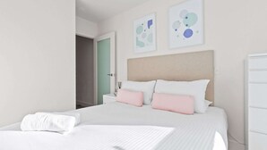 A hotel room with a large bed, white bedding, a beige headboard, and two abstract art pieces on the wall. - City View 2BR, FREE Parking, Bright & Central Apt (Melbourne)