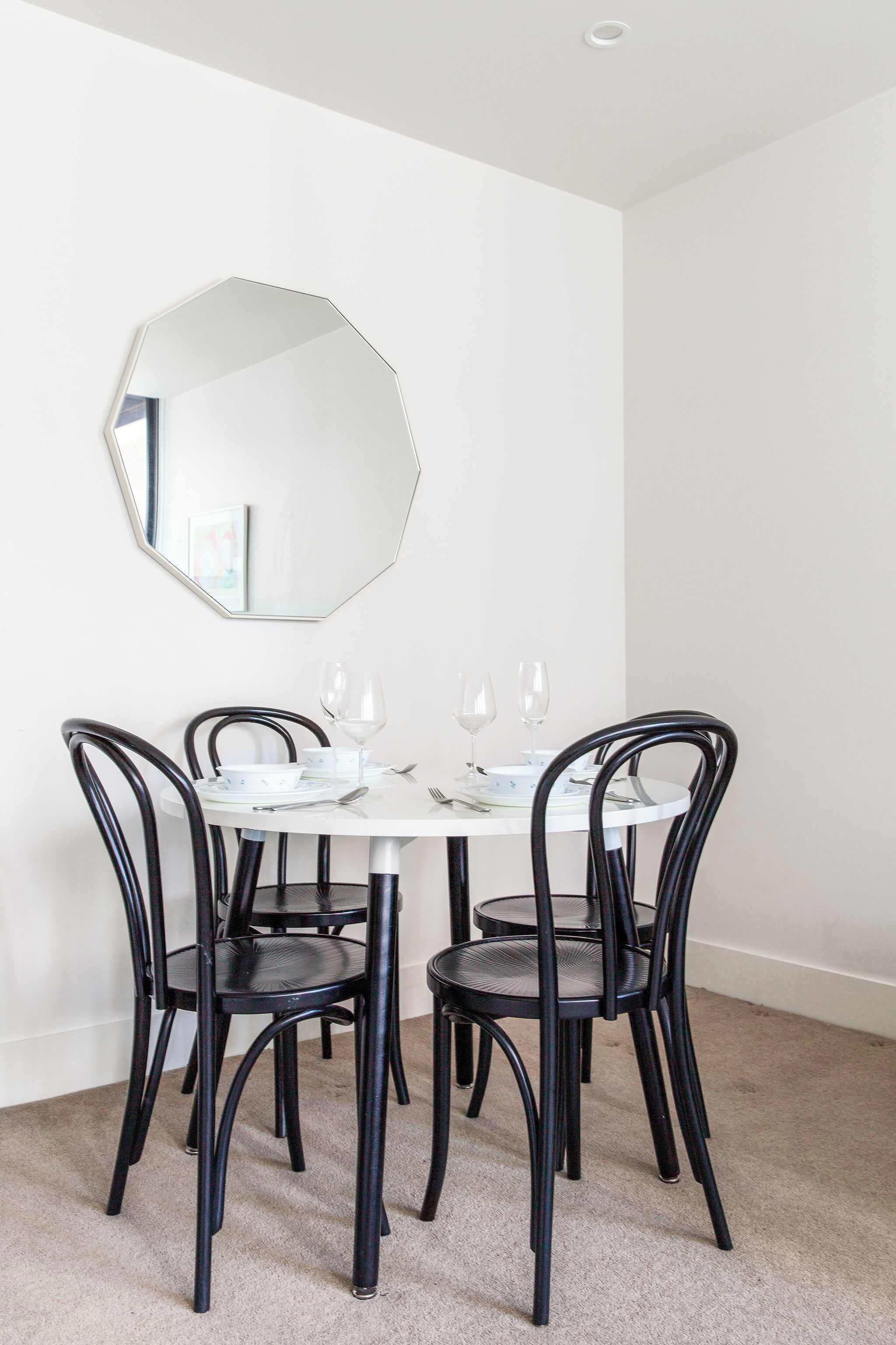 A dining area with a round table, four chairs, and a large mirror on the wall.