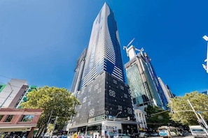 A modern high-rise building with a prominent glass facade, surrounded by other tall buildings and a busy street scene.