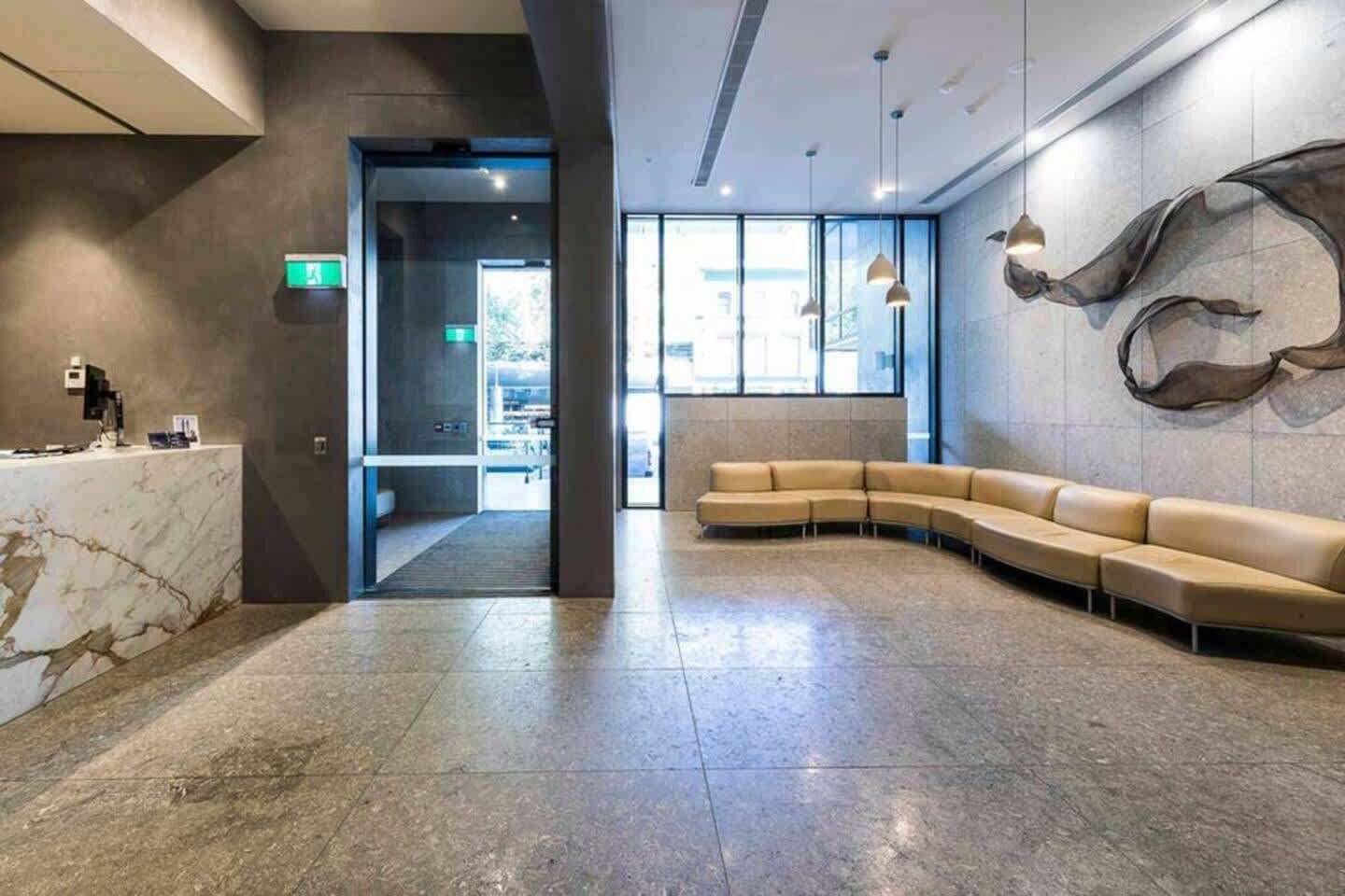 A modern lobby with a marble reception desk, a curved seating area, and a large abstract wall art piece.