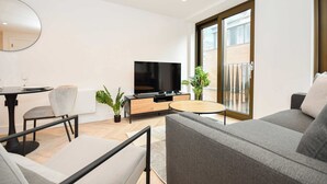 Uma sala de estar moderna com um sofá cinza, uma mesa de centro redonda, uma TV de tela plana e uma área de jantar com uma mesa e cadeiras.