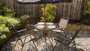 Une table ronde en métal, avec quatre chaises et un grand parasol.