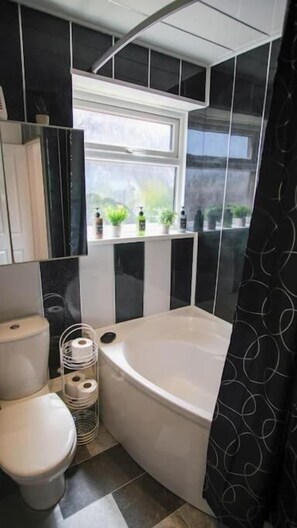 Un bagno con una vasca, un water e una finestra con piante.
