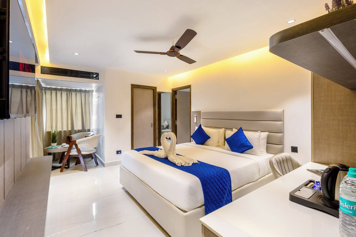 Une chambre d’hôtel moderne dotée d’un grand lit, d’un bureau, d’une chaise, d’un ventilateur de plafond et d’une grande fenêtre avec des rideaux.