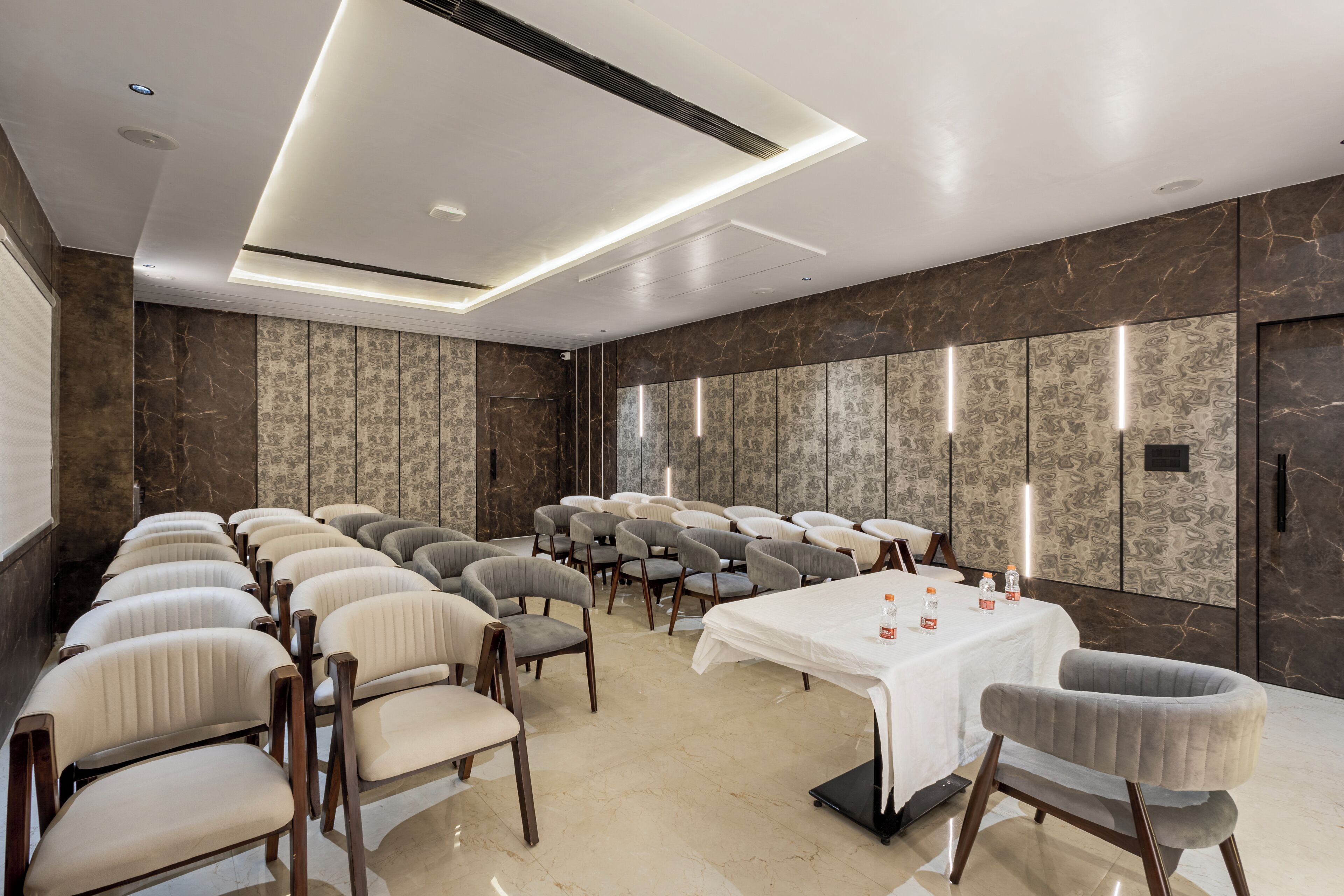 A conference room with rows of chairs, a table with water bottles, and a marble wall with a patterned design.