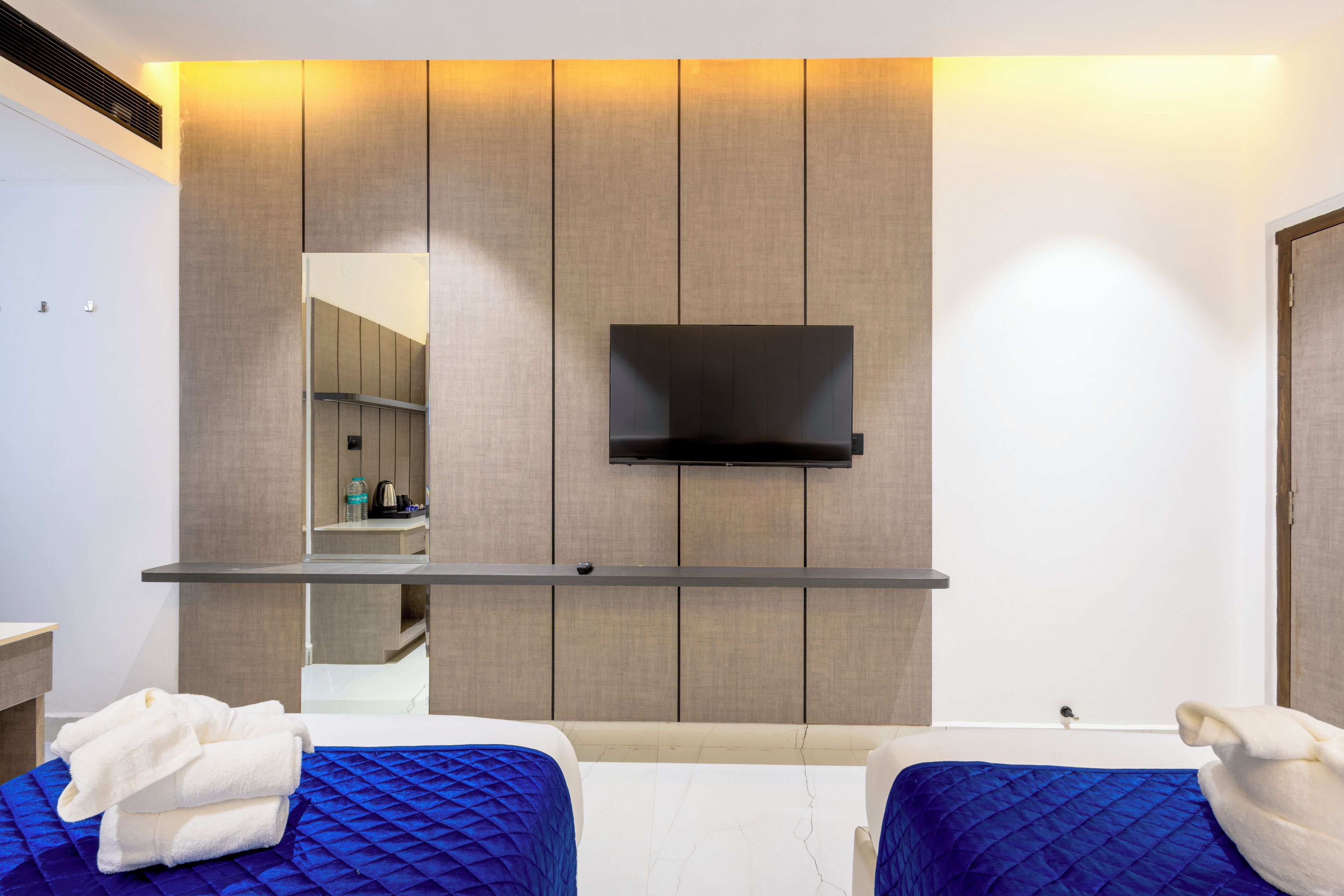Camera d'albergo con due letti, una TV a parete e uno specchio che riflette l'ambiente.