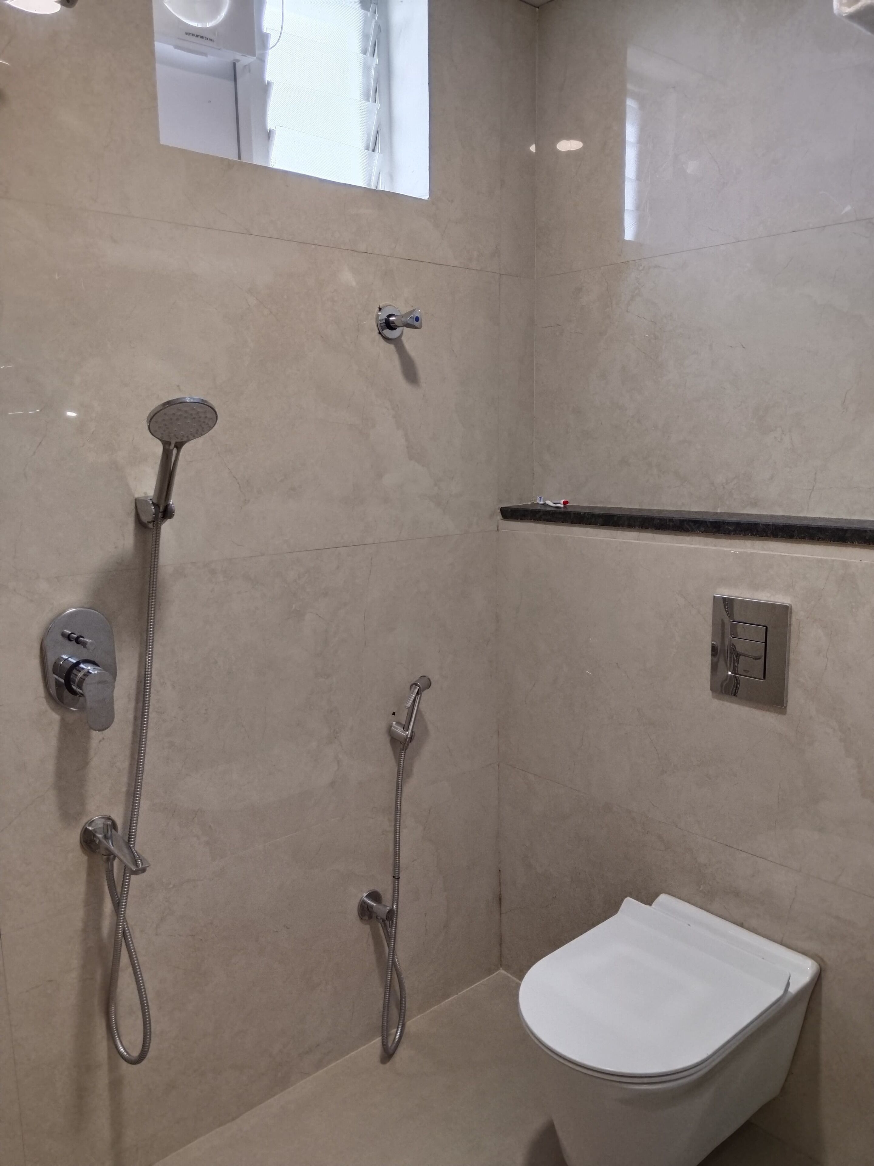 A modern bathroom with a shower, toilet, and a small window.