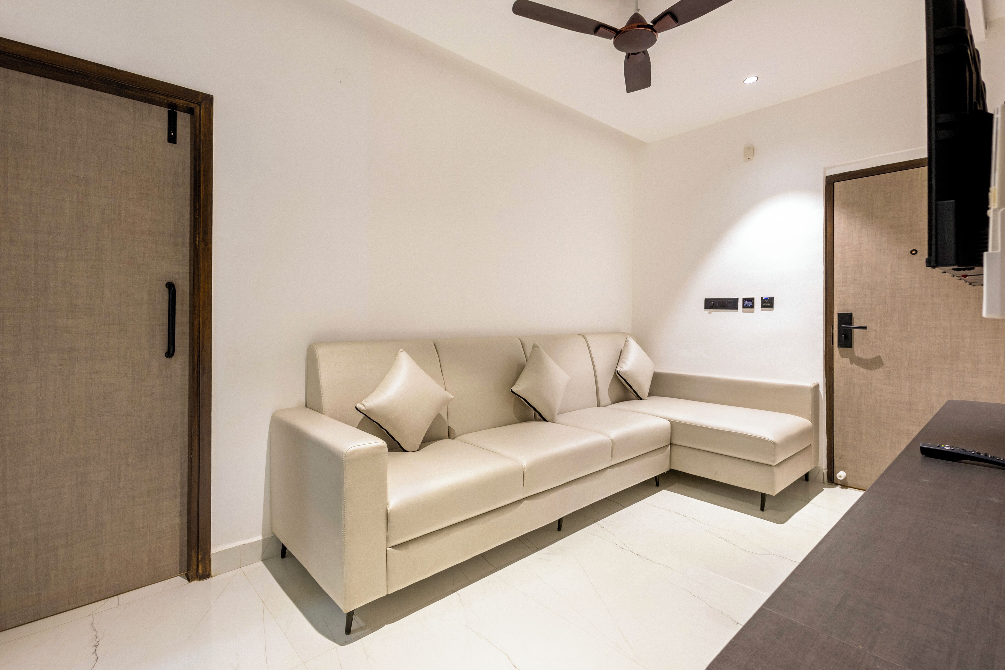 A modern living room with a beige sectional sofa, a ceiling fan, and a wooden door.