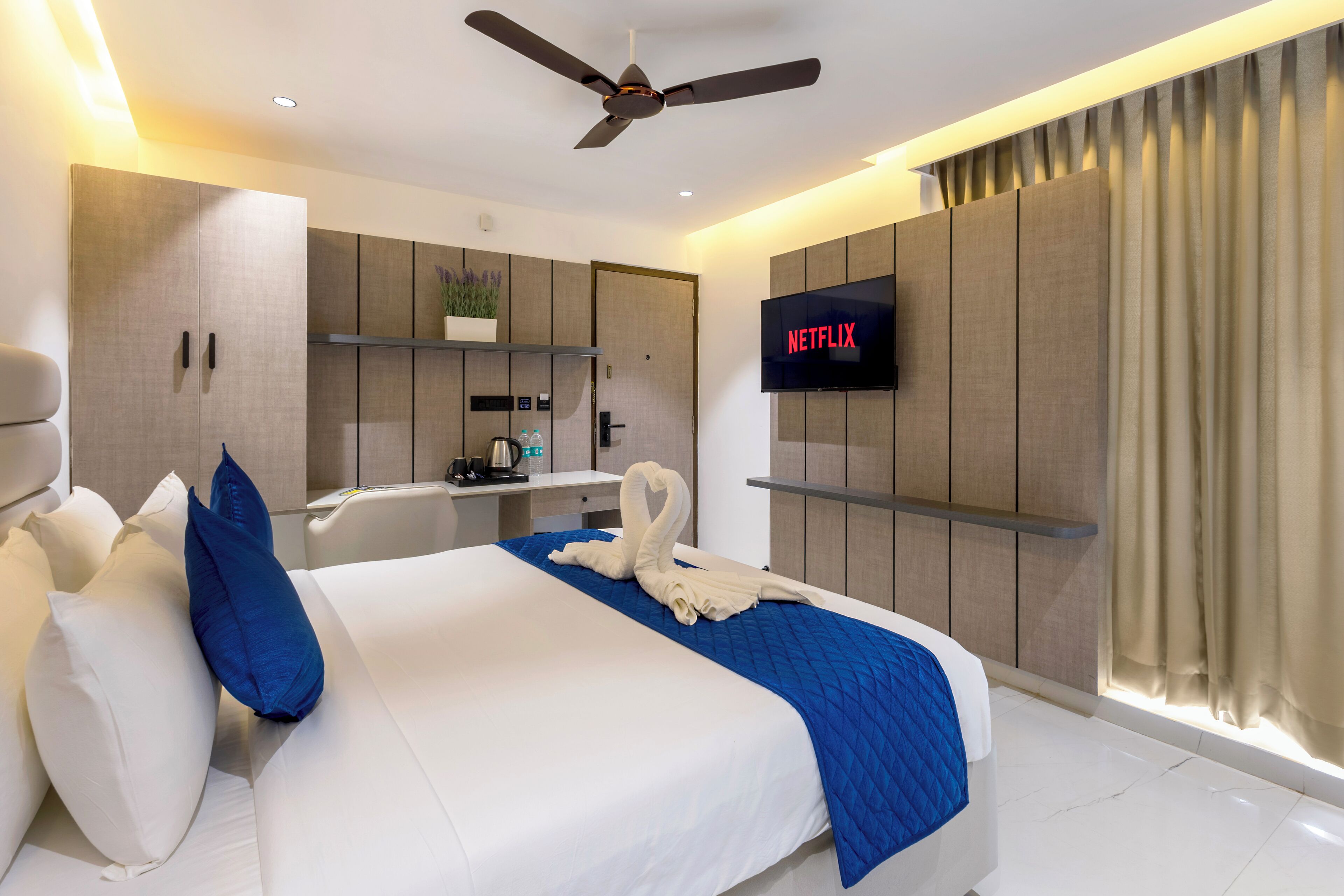 Una habitación de hotel moderna con cama, escritorio, televisor de pantalla plana y ventilador de techo.