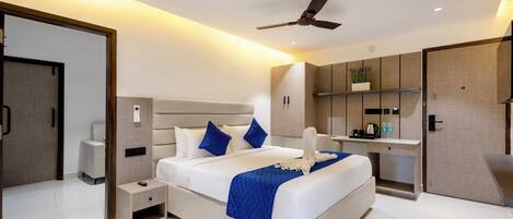 A modern hotel room with a large bed, a bedside table, a desk, and a wardrobe.