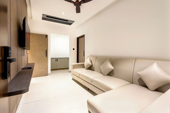 A modern living room with a sofa, a flat-screen TV mounted on the wall, and a ceiling fan. - ECKO La Maniere Business Hotels (Hyderabad)