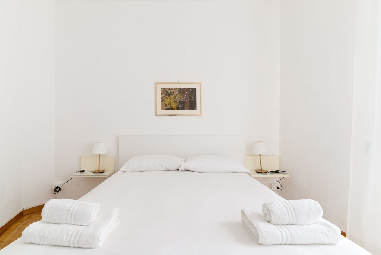 Habitación de hotel minimalista con una cama grande, dos mesitas de noche con lámparas y un cuadro en la pared.