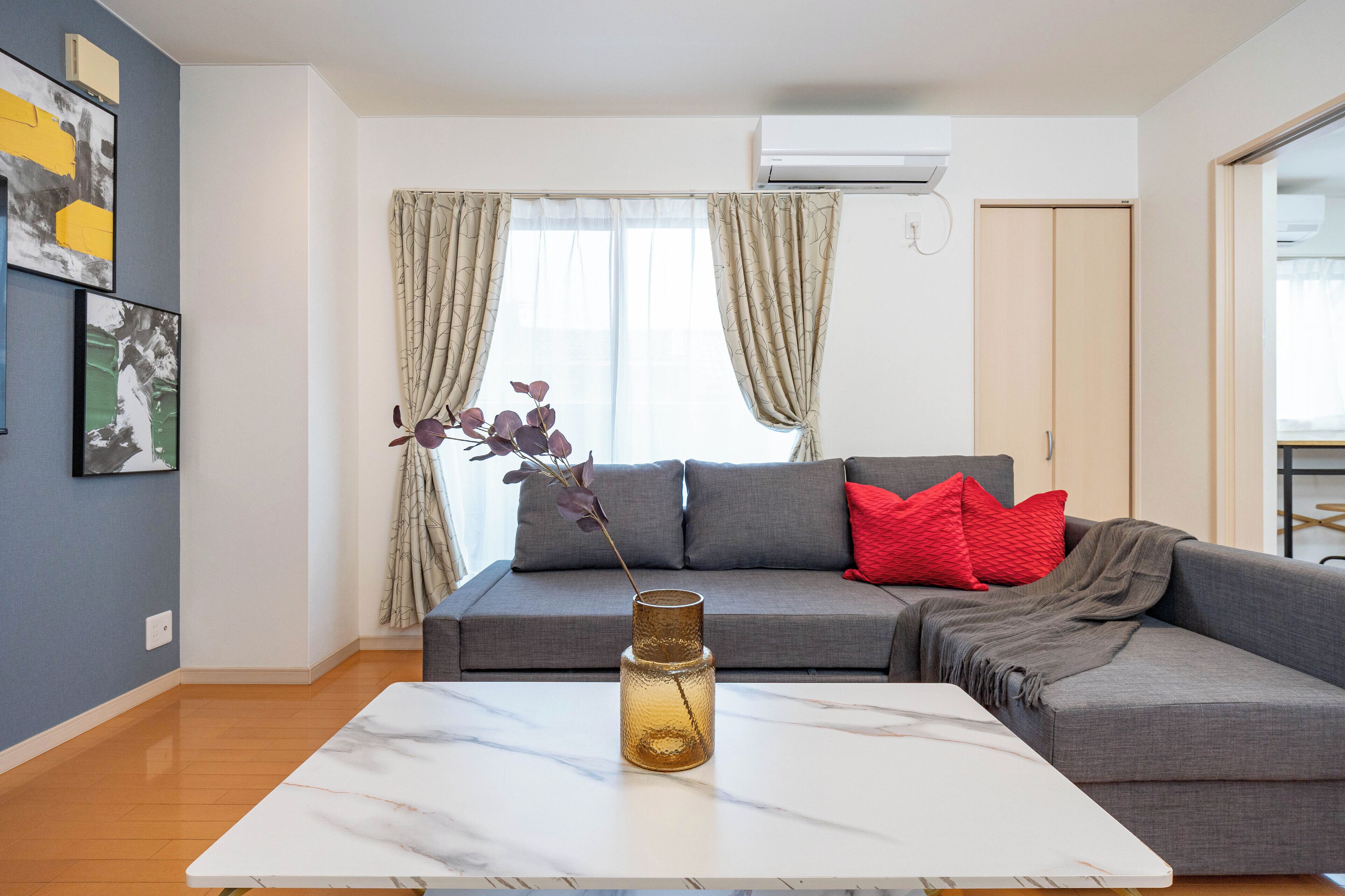A modern living room with a grey sofa, red pillows, a white coffee table, and a vase with flowers.