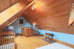 Une pièce avec un plafond en pente, des meubles en bois, une petite table et une chaise.